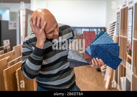 Der Mann wählt die Farbe des neuen Teppichs nach den Proben im Bodenbelaggeschäft Stockfoto