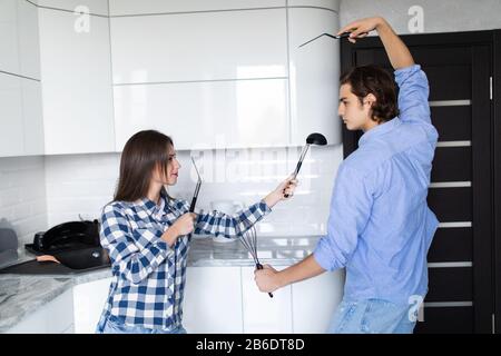 Lustige Paare, die vorgeben, mit Utensilien zu kämpfen, während sie zu Hause kochen, haben Mann und Frau Spaß dabei, spielerisch die küchen-stru zu halten Stockfoto