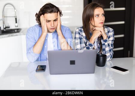 Porträt eines Familienpaares, das aufmerksam in den Bildschirm des Laptops schaut und am Küchentisch sitzt. Menschen, Zahlen, Budget Stockfoto