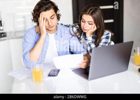 Junges Paar mit vielen Schulden, die gemeinsam Papierarbeiten, ihre Rechnungen prüfen, Familienbudget planen und Finanzen am Küchentisch mit PA berechnen Stockfoto