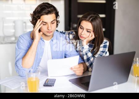 Junges Paar mit vielen Schulden, die gemeinsam Papierarbeiten, ihre Rechnungen prüfen, Familienbudget planen und Finanzen am Küchentisch mit PA berechnen Stockfoto