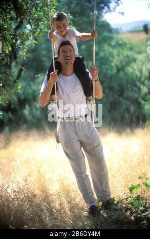 Ein Vater und sein Sohn auf einer Schaukel unter einem Baum. Stockfoto