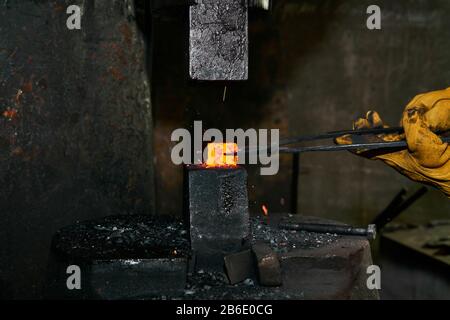 Woman Metal Artist verarbeitet ein rotes warmes Werkstück mit einem Krafthammer in einer Werkstatt Stockfoto