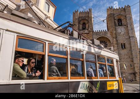 Lissabon, Portugal - 8. März 2020: Touristen, die die berühmte gelbe Straßenbahn 28 vor der Kathedrale von Lissabon fahren Stockfoto