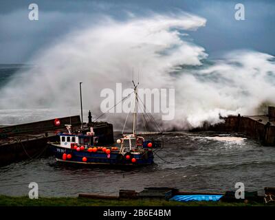 Eine Welle stürzt über die Hafenmauer und schützt ein Fischerboot in John o'Groats, Highlands, Schottland, Großbritannien, Europa Stockfoto