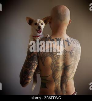 Ein tätowierter Mann trägt seinen Haustierhund. Stockfoto
