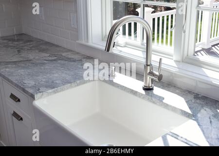 Modernes Küchenwaschbecken und Messingzapfhahn mit einem Griff mit Seifenspender, Marmor-Arbeitsplatte und Fenster zum Garten. Stockfoto