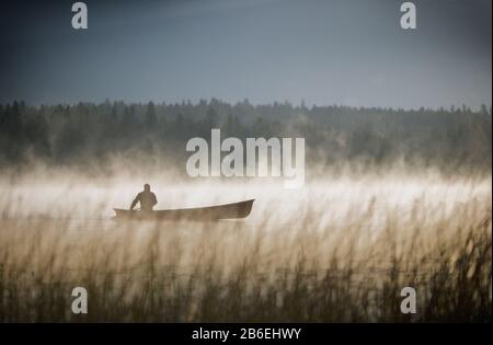 Mann im Kanu auf einem nebligen See Stockfoto