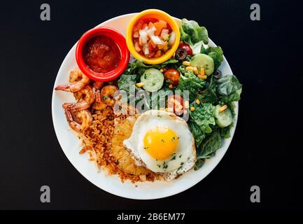 Asiatischer Ananas gebratener Reis mit verschiedenen Gemüsen auf weißem Teller und schwarzem Hintergrund Stockfoto