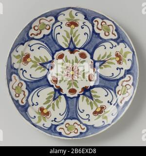 An Bord von Rond bord van veelkleurig beschilderde faience traf er in het midden een medaillon met daarin een bloem en bladerten in de kleuren groen en rood. Daar omheen zijn op een blauwe achtergrond vijf witte vakken Stockfoto