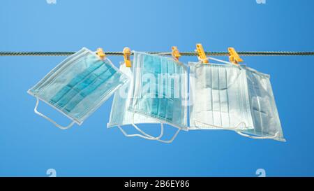 Medizinische Gesichtsmasken auf einer Wäscheleine mit Wäscheklappen im blauen Himmelshintergrund. Stockfoto