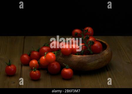 Frische Kirschtomaten auf schwarzem Hintergrund von der Seite gesehen, Frisch ganz und geschnitten (halbiert) rot tomatillos auf schwarzem Hintergrund von oben gesehen - fo Stockfoto