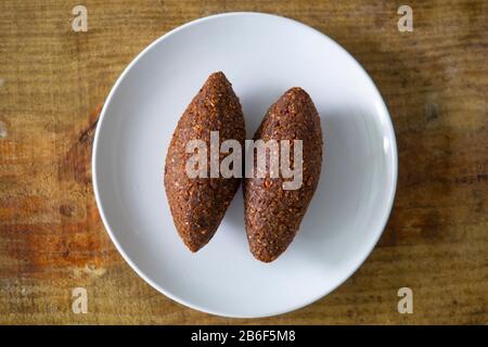 Quipe, delicioso kibbeh frito con salsa de yogur en un bol servido en un platon de arcilla sobre una vieja mesa de madera oscura, receta clásica, vista Stockfoto