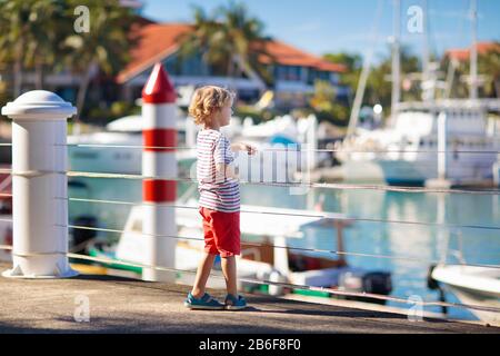 Kinder beobachten Yacht und Boot im Hafen. Segelsport für Familien mit Kindern. Kleiner Junge, der im Sommerurlaub in einem tropischen Resort spazieren geht. Nautische Fashi Stockfoto