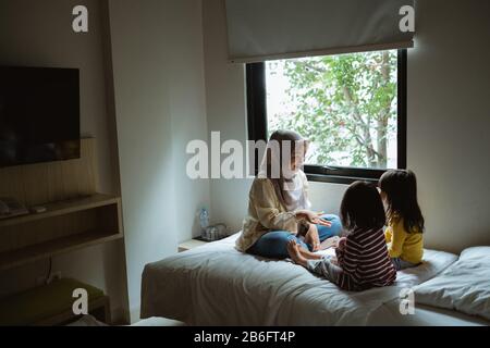 Die Mutter erzählt ihrer Tochter auf dem Bett, spielt zusammen Stockfoto