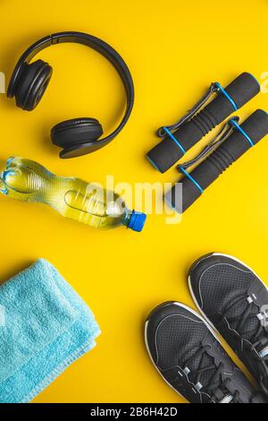 Fitnesskonzept. Schwarze Sportschuhe, Kopfhörer, Hanteln und eine Flasche Wasser auf gelbem Hintergrund. Draufsicht. Stockfoto