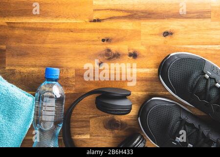 Fitnesskonzept. Schwarze Sportschuhe, Kopfhörer, Hanteln und eine Flasche Wasser auf Holzboden. Draufsicht. Stockfoto