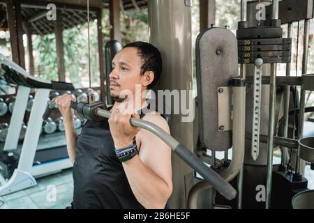 Asiatischer junger Mann, der Brustübungen mit einer Lat-Pulldown-Maschine im Firnhaus macht Stockfoto