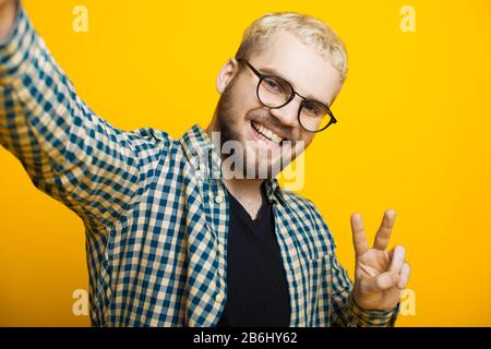 Nahaufnahme des Porträts eines kaukasischen Mannes mit blondem Haar und kurzem Bart, der durch Brillen blickt und ein selfie macht Stockfoto