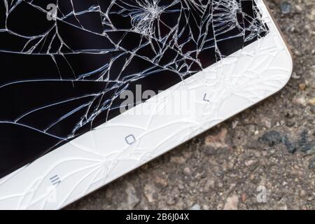 Smartphone mit kaputtem blauem Display liegt auf dem Asphalt. Nahaufnahme, selektiver Fokus Stockfoto