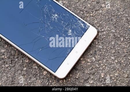 Smartphone mit kaputtem blauem Display liegt auf dem Asphalt. Nahaufnahme, selektiver Fokus Stockfoto