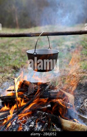 Camping im Freien - Kochen von Speisen auf dem Lagerfeuer im Wald. Kessel in der Natur in Brand Stockfoto