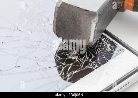 Auf dem Smartphone befindet sich ein Hammer mit einem defekten Bildschirm. Das Konzept der Elektronikreparatur. Nahaufnahme, selektiver Fokus Stockfoto