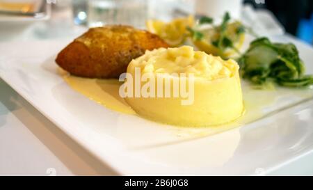 Gekochte Kartoffelpüree, Kürbis, grüner Salat und Zitronen auf einem weißen Teller in einem Restaurant. Selektiver, weicher Fokus. Nahaufnahme. Drinnen. Stockfoto