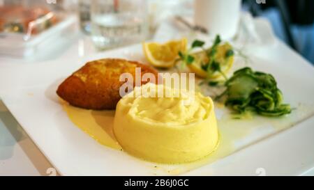 Gekochte Kartoffelpüree, Kürbis, grüner Salat und Zitronen auf einem weißen Teller in einem Restaurant. Selektiver, weicher Fokus. Nahaufnahme. Drinnen. Stockfoto