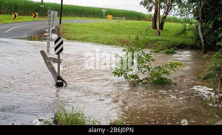 Wasser über die Straße von einem überströmten Bach, der durch starke tropische Regenfälle verursacht wird. Das Vorzeichen zeigt die Tiefe an. Stockfoto