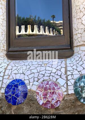 Zerbrochene Glasmosaikfliesen als Keramikkunst an der Gebäudewand und Spiegelung des Glasfensters im Park Guell, Barcelona, Spanien Stockfoto