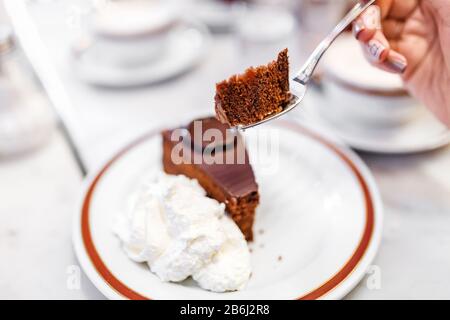 Eine Frau, die in einem Café eine Gabel isst, ist ein köstlicher und schmackhafter Sacher-Kuchen Stockfoto