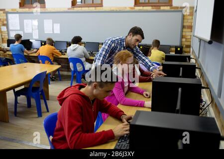 Seitenansicht des Lehrers, der Schülern auf dem Computer hilft Stockfoto