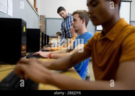 Seitenansicht des Lehrers, der Schülern auf dem Computer hilft Stockfoto