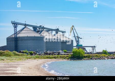 Große Körnerelevatorsilos im Hafen mit fliegenden Vögeln und Meeresküste (Hafen von Liepaja, Lettland) Stockfoto