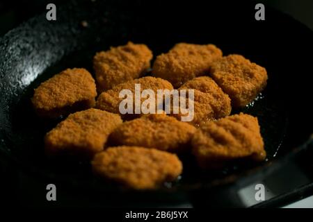 Goldene Huhn Nuggets Frittieren in heißem Öl schwarze dunkle Pfanne Stockfoto