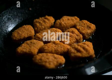 Goldene Huhn Nuggets Frittieren in heißem Öl schwarze dunkle Pfanne Stockfoto