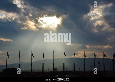 Sonnenlicht, das durch ein Loch in Wolken über Flagpolen kommt Stockfoto