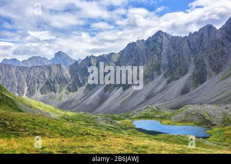 Sibirische alpine Tundra vor dem Hintergrund der Bergkette. Eine charakteristische alpine Landschaft mit spärlicher Vegetation in Ostsibirien. Trogtal Stockfoto