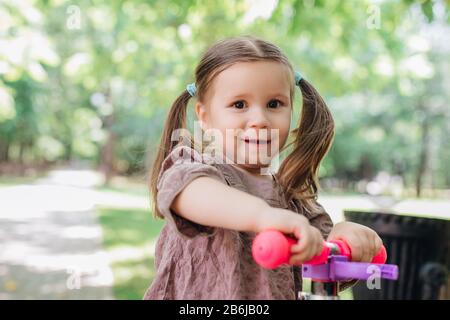 Niedlicher kleiner Kleinkind mit Roller im Stadtpark Stockfoto