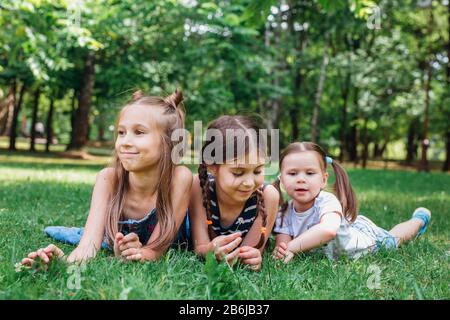 Gruppe glücklicher Kinder, die im Frühlingspark auf grünem Gras liegen Stockfoto