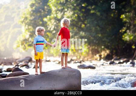 Kinder, die in den Alpen wandern, überqueren den Fluss. Kinder spielen auf dem Berg in Österreich im Wasser. Familienurlaub im Frühling. Kleiner Junge auf Wanderpfad. Im Freien Stockfoto