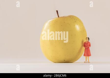 Miniaturfigur der Frau neben dem großen gelben apfel stehend. Geringe Tiefe des Feldhintergrunds. Gesundheitswesen, gesunder Lebensstil und schlankes Konzept. Stockfoto