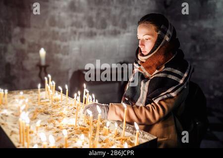 Junge Frau zündet beim Beten Kerzen in einer Kirche an. Stockfoto