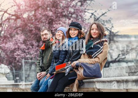Eine multirassische Gruppe junger Menschen, die sich in einem Frühlingspark gegen eine blühende Kirschblüte lustig machen Stockfoto