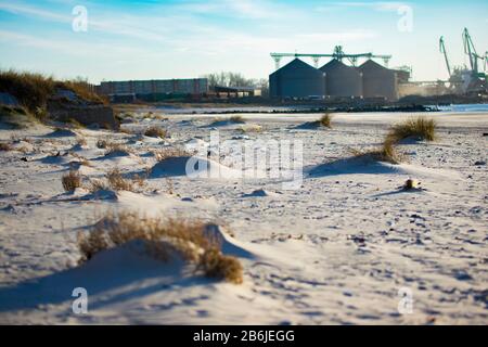 Strand mit Industriehafen im Hintergrund. Silos und Kräne (Hafen von Liepaja, Lettland) Stockfoto