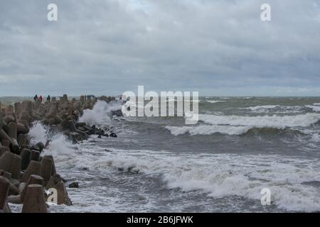 Wellen, die gegen Wellenbrecher aus grauen Betontetrapoden krachen. Liepaja, Lettland. Stockfoto