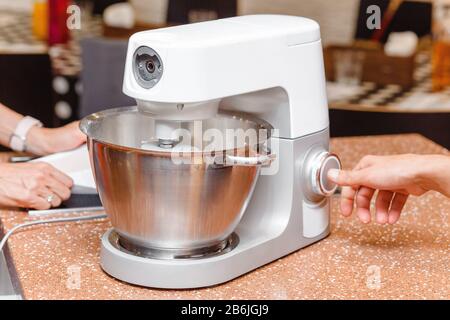 Frau, die in der Schürze mit einem Mixer oder einer Küchenmaschine zum Kneten von Teig kocht Stockfoto