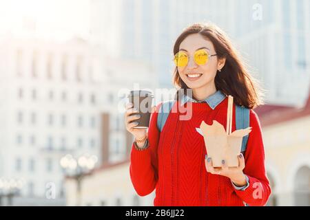 Nahaufnahme der jungen asiatischen Frau mit Kaffeetasse und Wok Nudeln Papierbox auf der Straße der Stadt Stockfoto