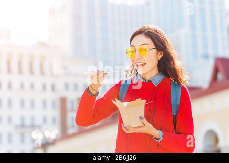 Happy Girl, das asiatische Wok fast Food aus dem Papierkiste zum Mitnehmen an der Straße der Stadt isst, Student oder Arbeiter Mittagspause Konzept Stockfoto